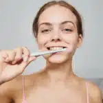 Smiling woman brushing teeth with toothbrush, promoting dental hygiene and oral health.