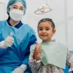 Dentist and child patient giving thumbs up in dental office, emphasizing pediatric dental care and positive patient experience.