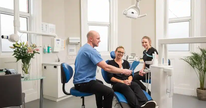 Dental consultation scene with a dentist discussing treatment options with a patient and a dental assistant in a modern clinic setting.