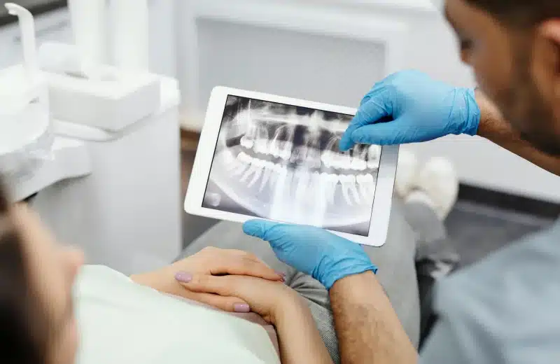 Dentist showing dental X-ray on tablet to patient in dental office, highlighting oral surgery options and treatment planning.