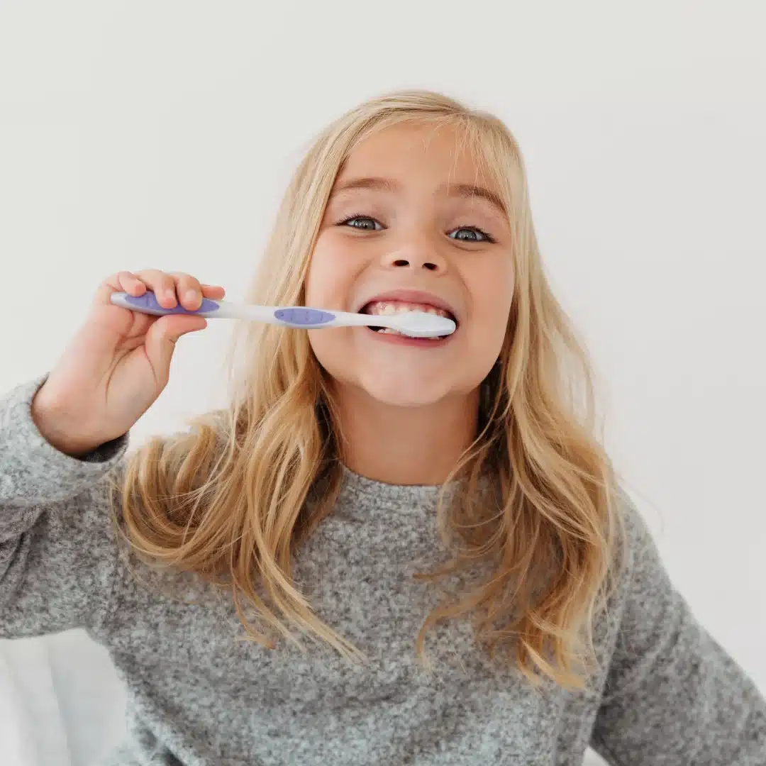 Smiling girl brushing her teeth with a toothbrush, promoting good dental hygiene and oral health care.