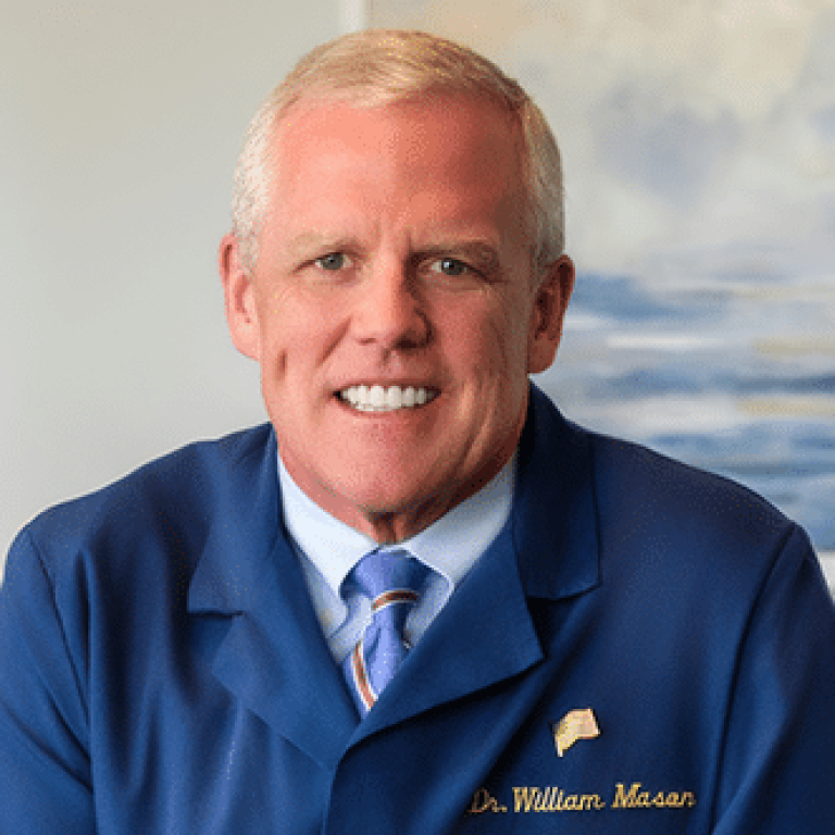 Dr. William Mason smiling in a blue dental coat, showcasing his expertise as a periodontist in Bay City, Michigan.