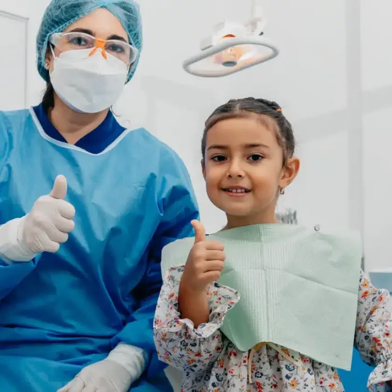 Child and pediatric dentist giving thumbs up in dental office, promoting positive children's dentistry experience and smile makeovers.